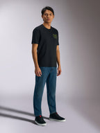 Alpinestars Order CSF Tee, t-shirt a maniche corte, nero, con loghi verdi di casco e palme sul petto, streetwear casual motorsport, indossata con jeans blu e sneakers nere