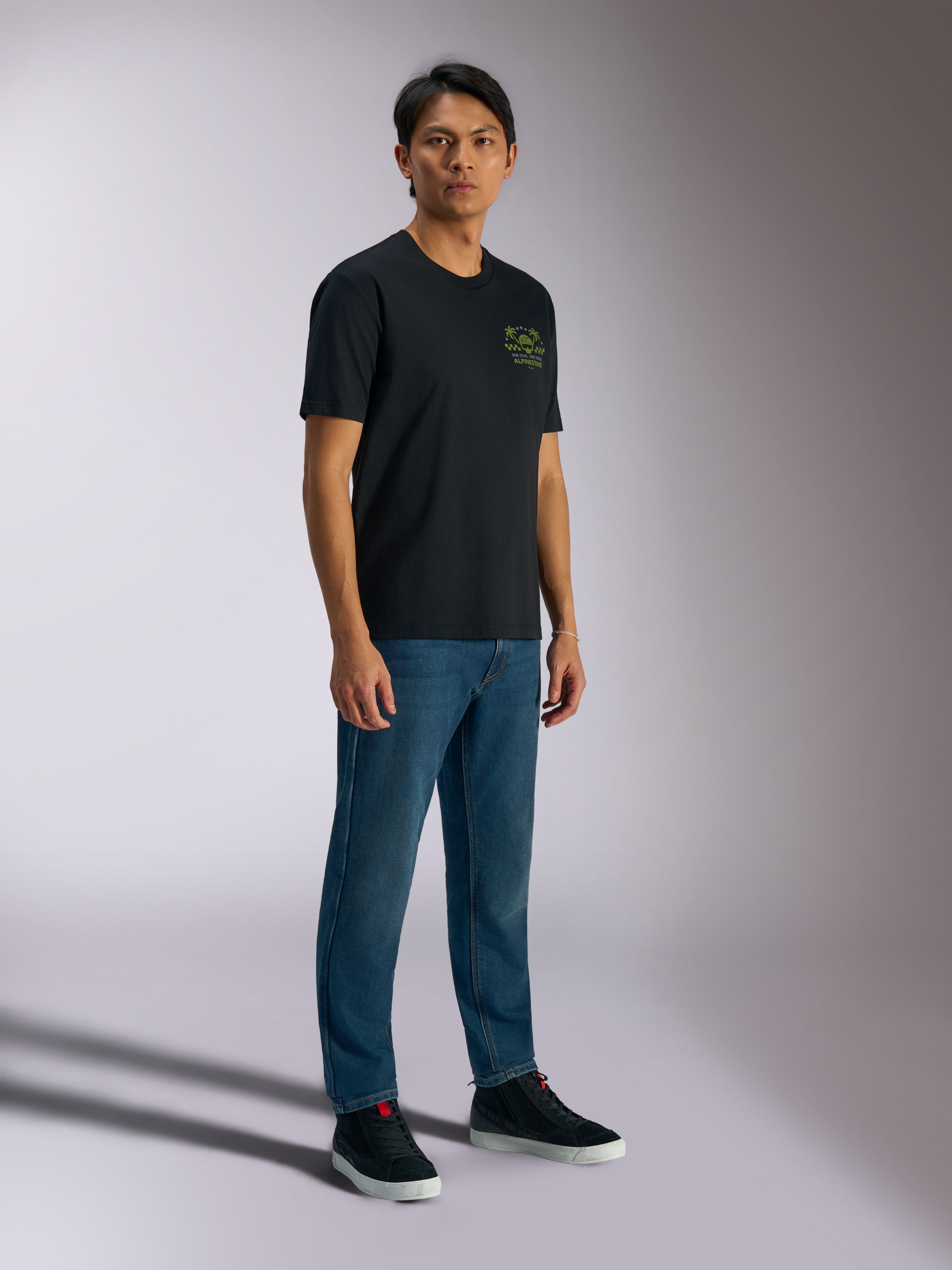 Alpinestars Order CSF Tee, t-shirt a maniche corte, nero, con loghi verdi di casco e palme sul petto, streetwear casual motorsport, indossata con jeans blu e sneakers nere