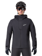 Giacca Alpinestars A-Dura Elite Waterproof, nero, giacca da mountain bike, design a collo alto con cappuccio, cerniera frontale con patta protettiva sul petto e logo bianco, indossata con casco nero e guanti da ciclismo, protezione tecnica contro le intemperie per il trail riding