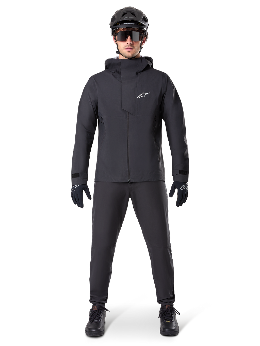 Giacca impermeabile Alpinestars A-Dura Elite, colore nero, indossata con pantaloni da ciclismo e guanti coordinati, casco e occhiali da sole neri, con logo Astars bianco sul petto, design tecnico ad alte prestazioni per mountain bike