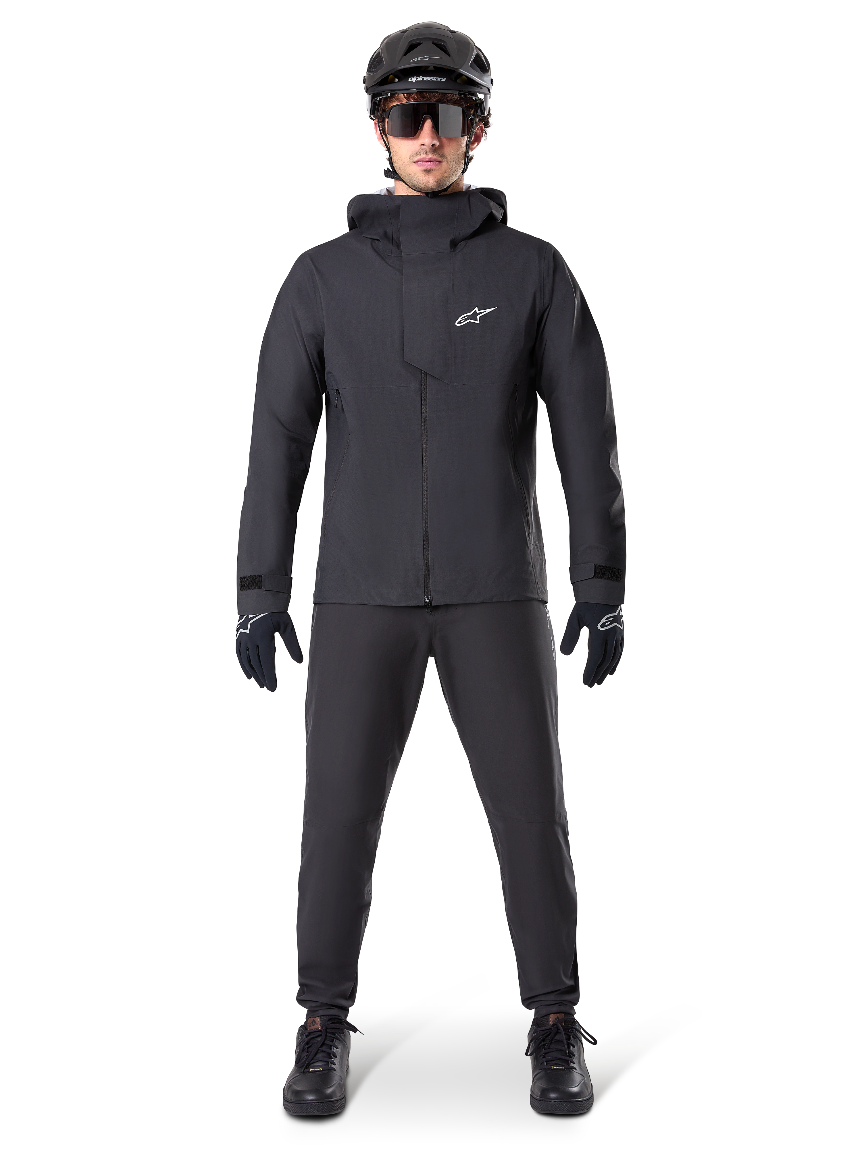 Giacca impermeabile Alpinestars A-Dura Elite, colore nero, indossata con pantaloni da ciclismo e guanti coordinati, casco e occhiali da sole neri, con logo Astars bianco sul petto, design tecnico ad alte prestazioni per mountain bike