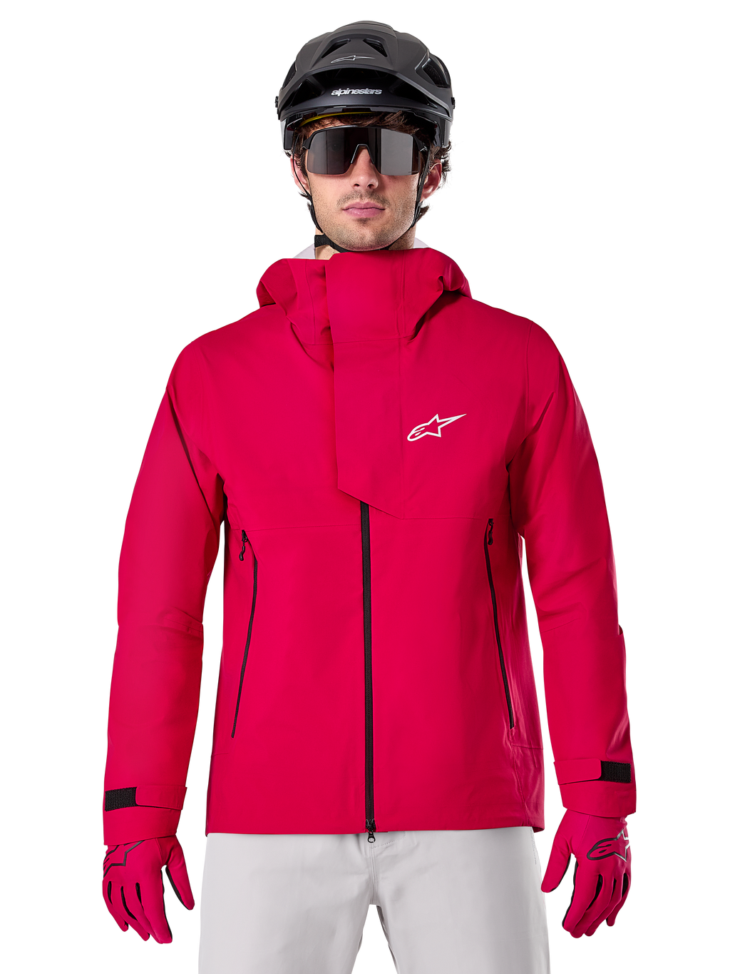 Alpinestars A-Dura Elite Waterproof Jacket, giacca antipioggia per mountain bike, rosso fluo, collo alto con logo Alpinestars bianco, dettagli con zip nera, indossata con guanti coordinati e casco da ciclismo nero, abbigliamento tecnico impermeabile da ciclismo