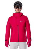 Alpinestars A-Dura Elite Waterproof Jacket, giacca antipioggia per mountain bike, rosso fluo, collo alto con logo Alpinestars bianco, dettagli con zip nera, indossata con guanti coordinati e casco da ciclismo nero, abbigliamento tecnico impermeabile da ciclismo