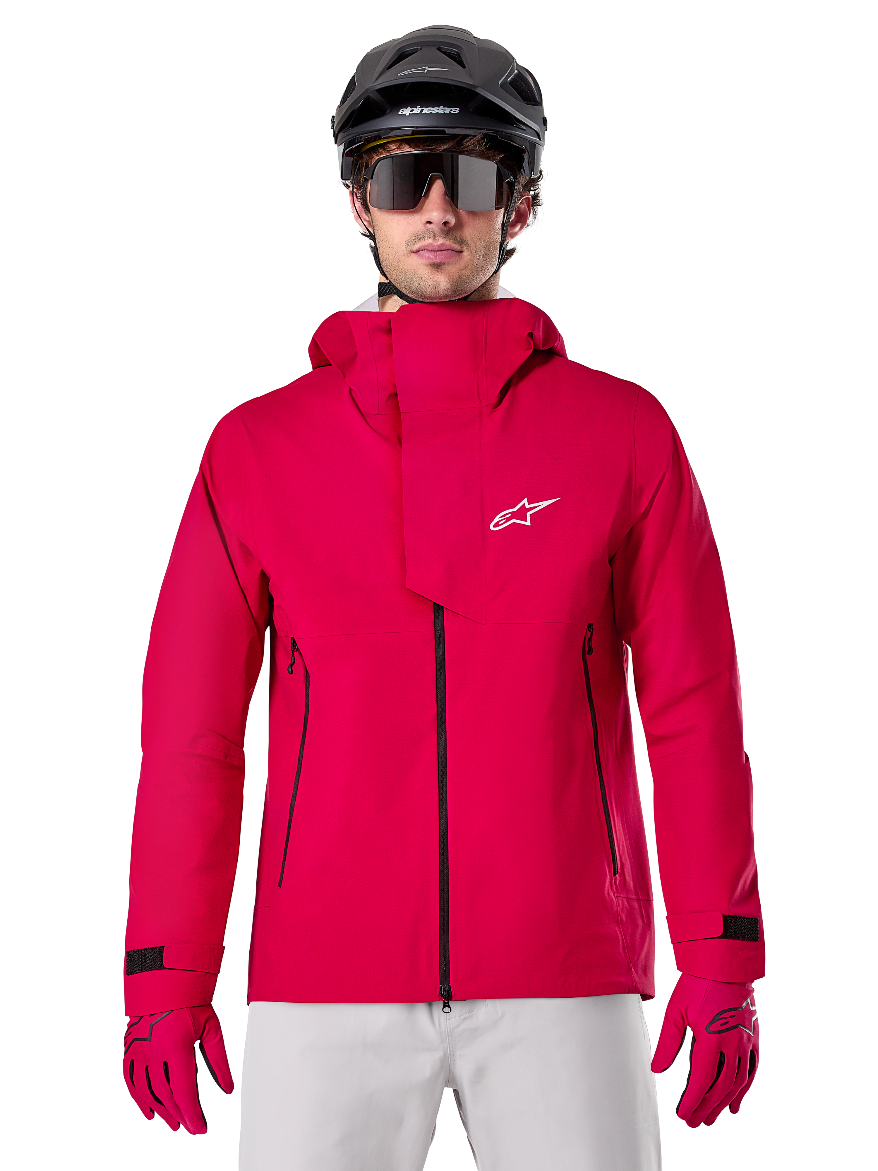 Alpinestars A-Dura Elite Waterproof Jacket, giacca antipioggia per mountain bike, rosso fluo, collo alto con logo Alpinestars bianco, dettagli con zip nera, indossata con guanti coordinati e casco da ciclismo nero, abbigliamento tecnico impermeabile da ciclismo