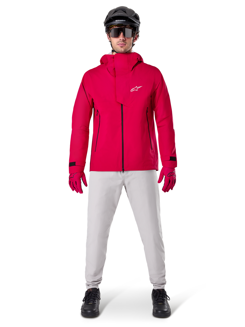 Giacca impermeabile Alpinestars A-Dura Elite, Rosso Fluo, giacca tecnica da mountain bike indossata con un casco da MTB nero, occhiali da sole, guanti rossi coordinati e pantaloni grigio chiaro, vista a figura intera dell'abbigliamento da ciclismo per tutte le condizioni atmosferiche