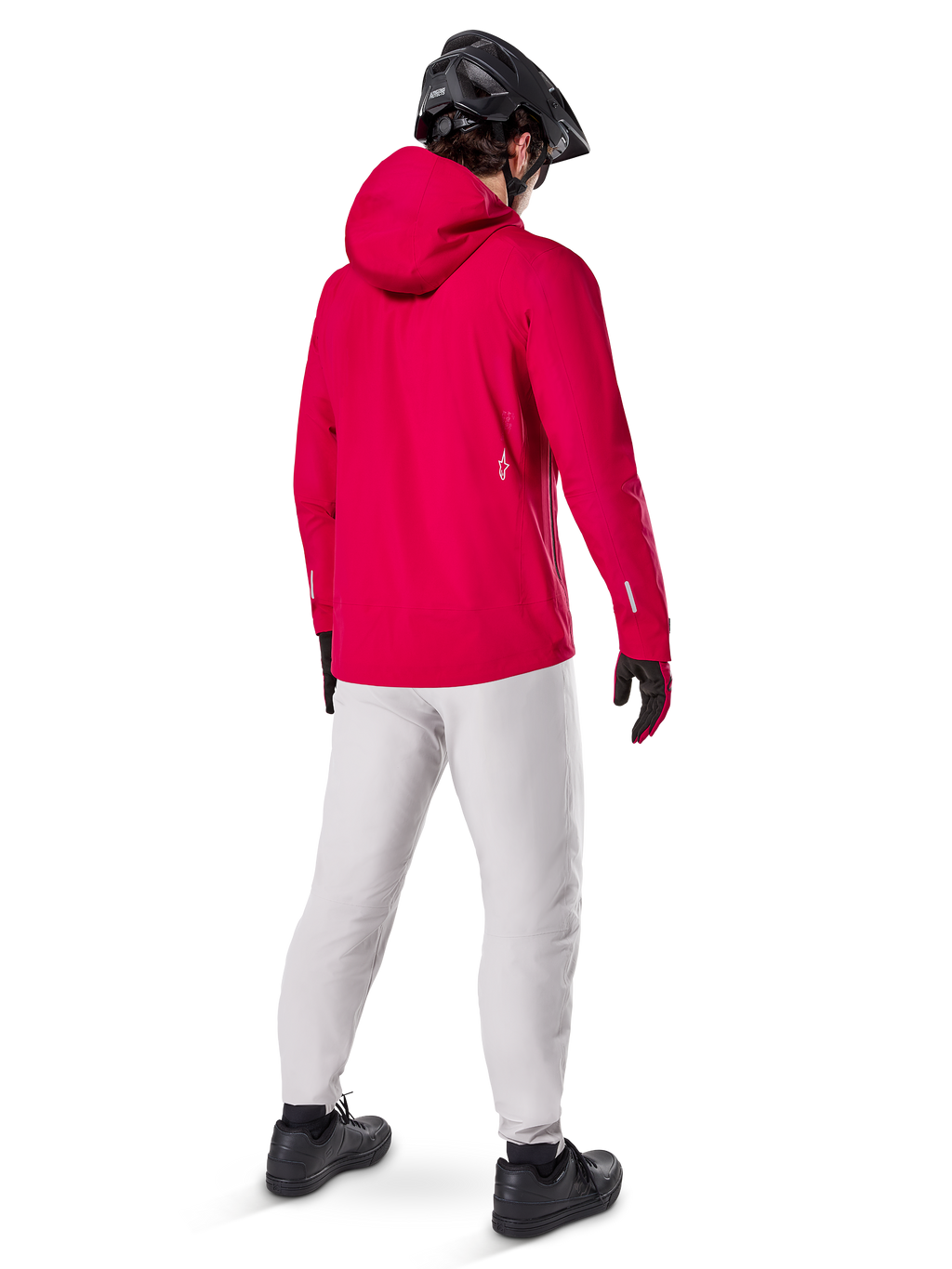 Alpinestars Giacca Impermeabile A-Dura Elite, Rosso Fluo, vista posteriore a tre quarti, indossata con pantaloni grigio chiaro e casco MTB nero, dotata di cappuccio e dettagli riflettenti, giacca antipioggia da ciclismo ad alte prestazioni per trail riding