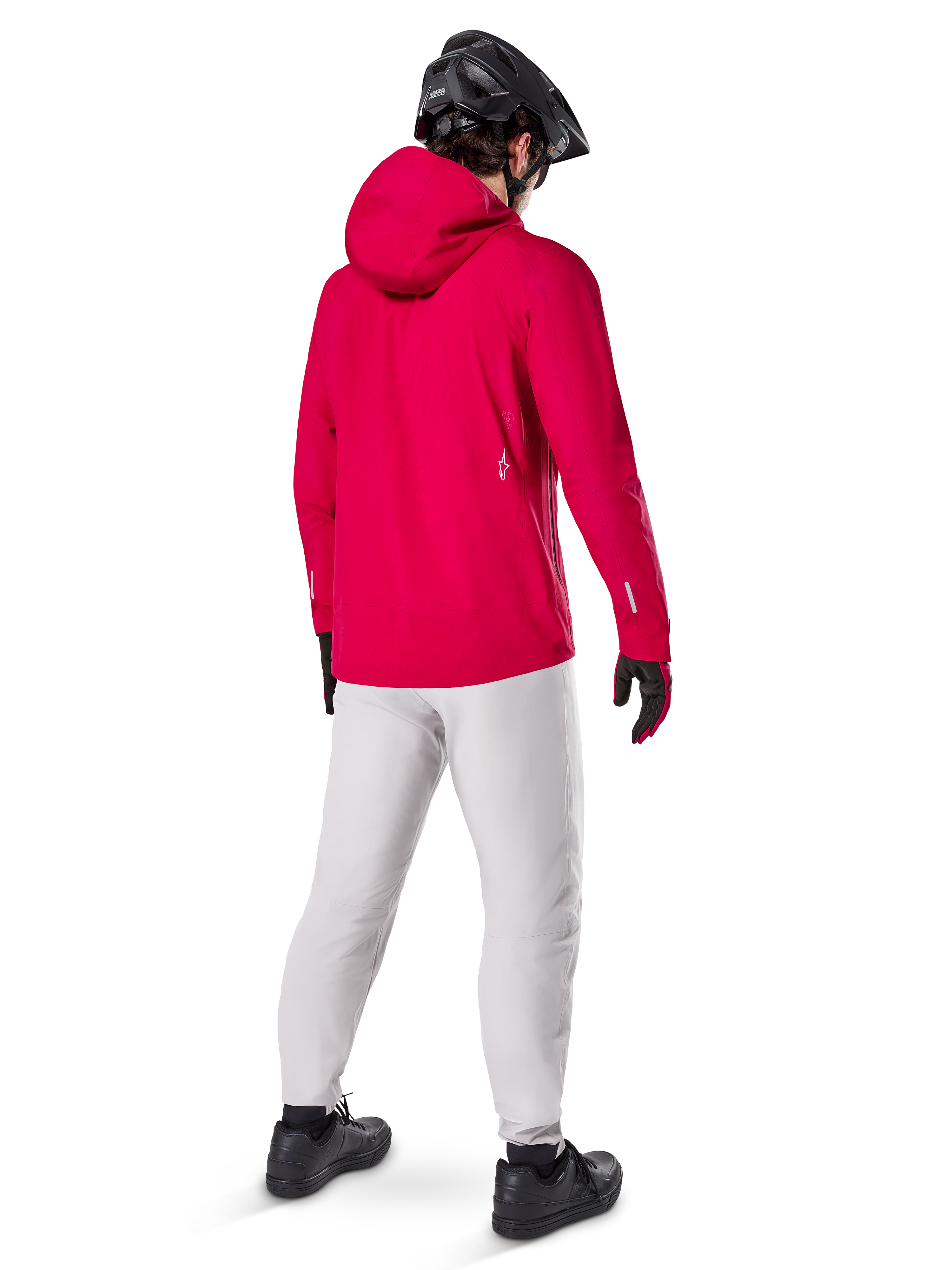 Alpinestars Giacca Impermeabile A-Dura Elite, Rosso Fluo, vista posteriore a tre quarti, indossata con pantaloni grigio chiaro e casco MTB nero, dotata di cappuccio e dettagli riflettenti, giacca antipioggia da ciclismo ad alte prestazioni per trail riding