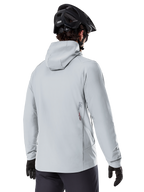 Giacca Termica Alpinestars A-Dura, Grigio Titanio, vista posteriore di un rider che indossa la giacca isolata con cappuccio, abbinata a un casco MTB nero e guanti neri, con un piccolo logo Alpinestars sulla parte inferiore della schiena, progettata per mountain bike in condizioni di freddo