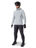 Giacca termica Alpinestars A-Dura in Titanium, giacca da ciclismo grigio chiaro con cappuccio e logo Alpinestars rosso sul petto, indossata da un uomo con casco da MTB nero, occhiali da sole, pantaloni grigio scuro e guanti neri, attrezzatura professionale da mountain bike
