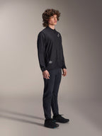 Giacca frangivento Alpinestars A-Aria, nera, giacca da ciclismo leggera e resistente al vento indossata da un modello con capelli ricci, con logo Astars bianco sul petto e marchio in basso a destra, abbinata a pantaloni e scarpe neri, vestibilità performante per mountain bike e gravel
