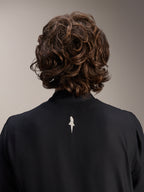 Giacca Frangivento Alpinestars A-Aria, nero, vista posteriore ravvicinata della parte superiore delle spalle e del colletto, con un piccolo logo bianco al centro della schiena, indossata da un modello con capelli castani mossi, abbigliamento tecnico da ciclismo minimalista