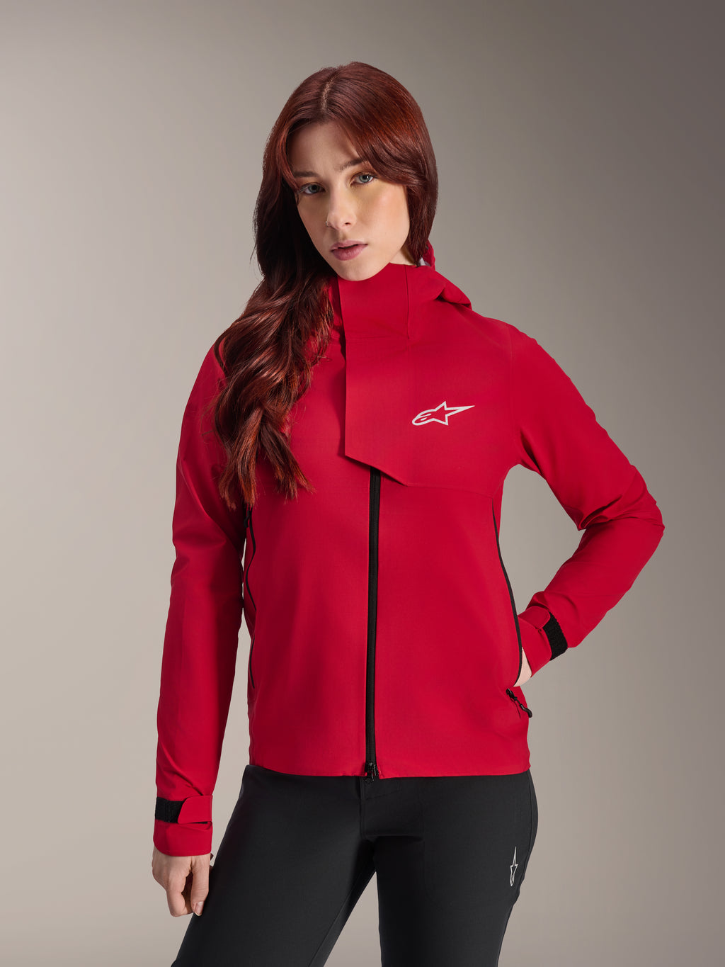Giacca impermeabile Alpinestars Stella A-Dura Elite, giacca da mountain bike da donna, Rosso Fluo, con patta antivento anteriore dotata di logo Alpinestars bianco, collo alto e polsini regolabili, indossata con pantaloni neri per un look tecnico da riding