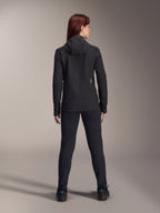 Donna con Giacca Termica Alpinestars Stella A-Dura, vista posteriore, giacca da ciclismo termica nera con cappuccio, pantaloni e scarpe neri coordinati, piccolo logo bianco sulla parte inferiore della schiena