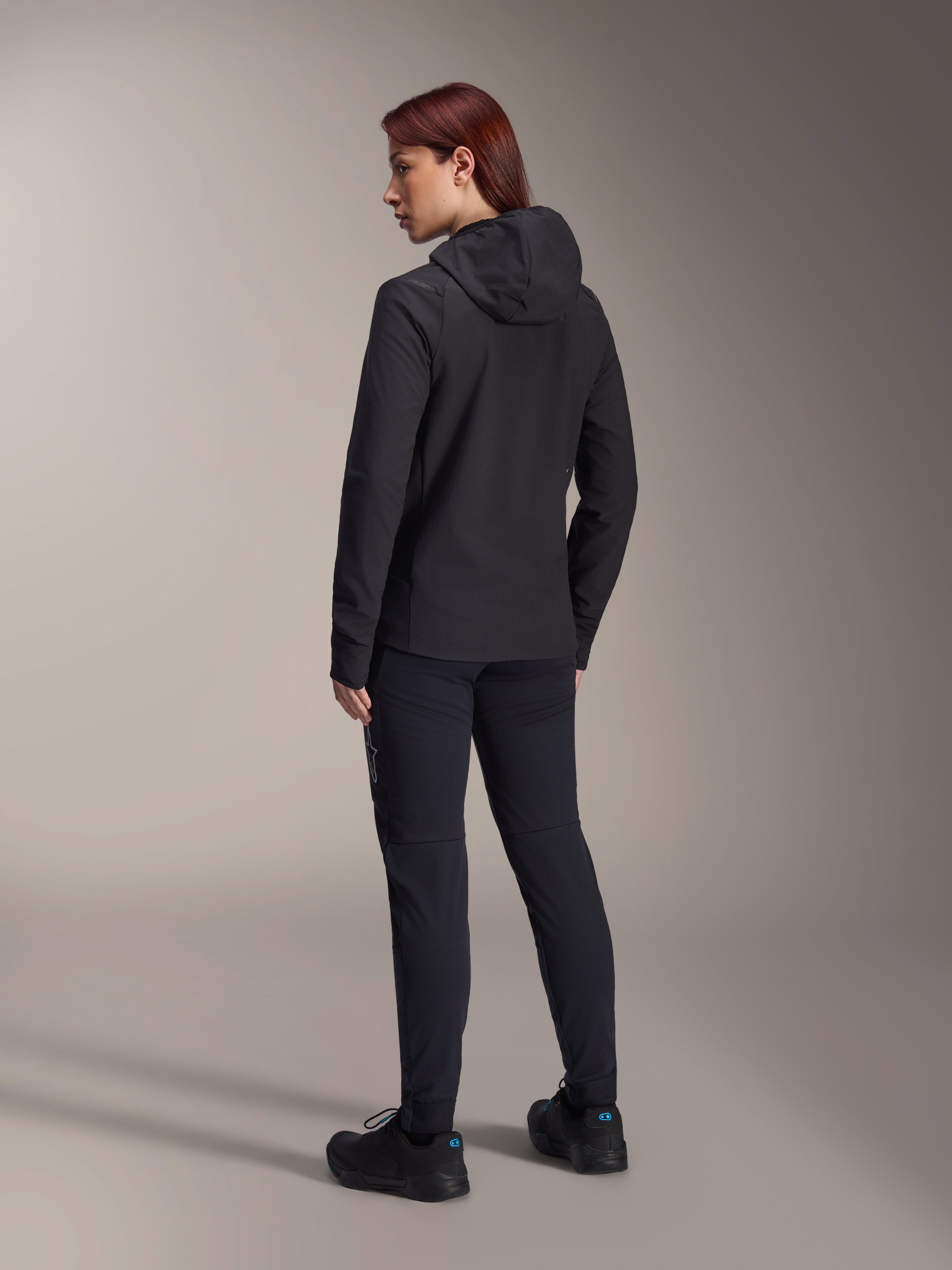Giacca Termica Stella A-Dura Alpinestars, giacca da ciclismo MTB da donna, nero, vista posteriore che mette in risalto il cappuccio isolato e la vestibilità regolare, indossata con pantaloni e scarpe neri coordinati, isolamento termico leggero per la guida in climi freddi