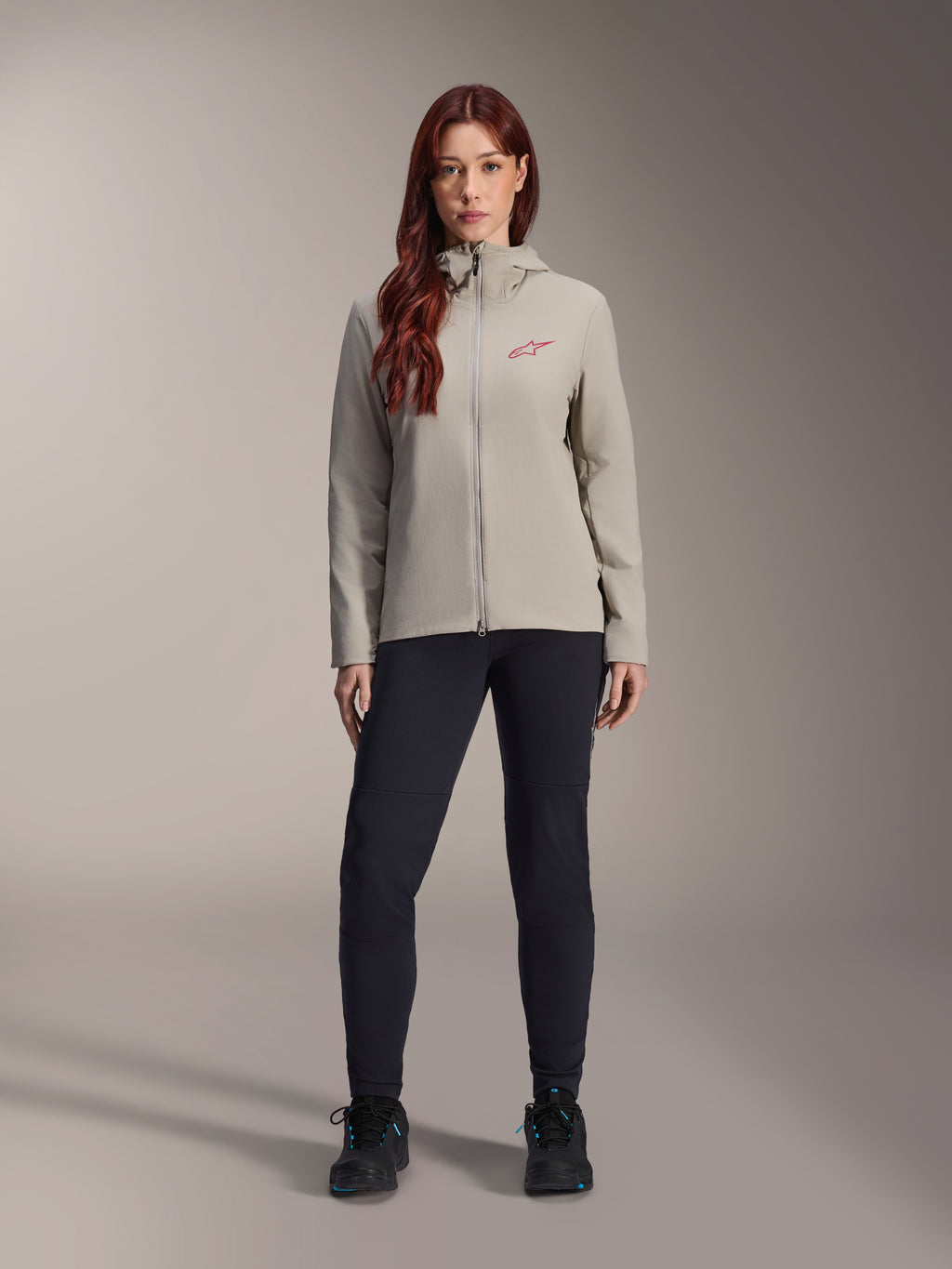 Giacca Termica Alpinestars Stella A-Dura da donna, giacca da mountain bike, grigio titanio, indossata con pantaloni tecnici neri e calzature nere, dotata di cappuccio foderato in pile e logo rosso sul petto, progettata per la guida in climi freddi