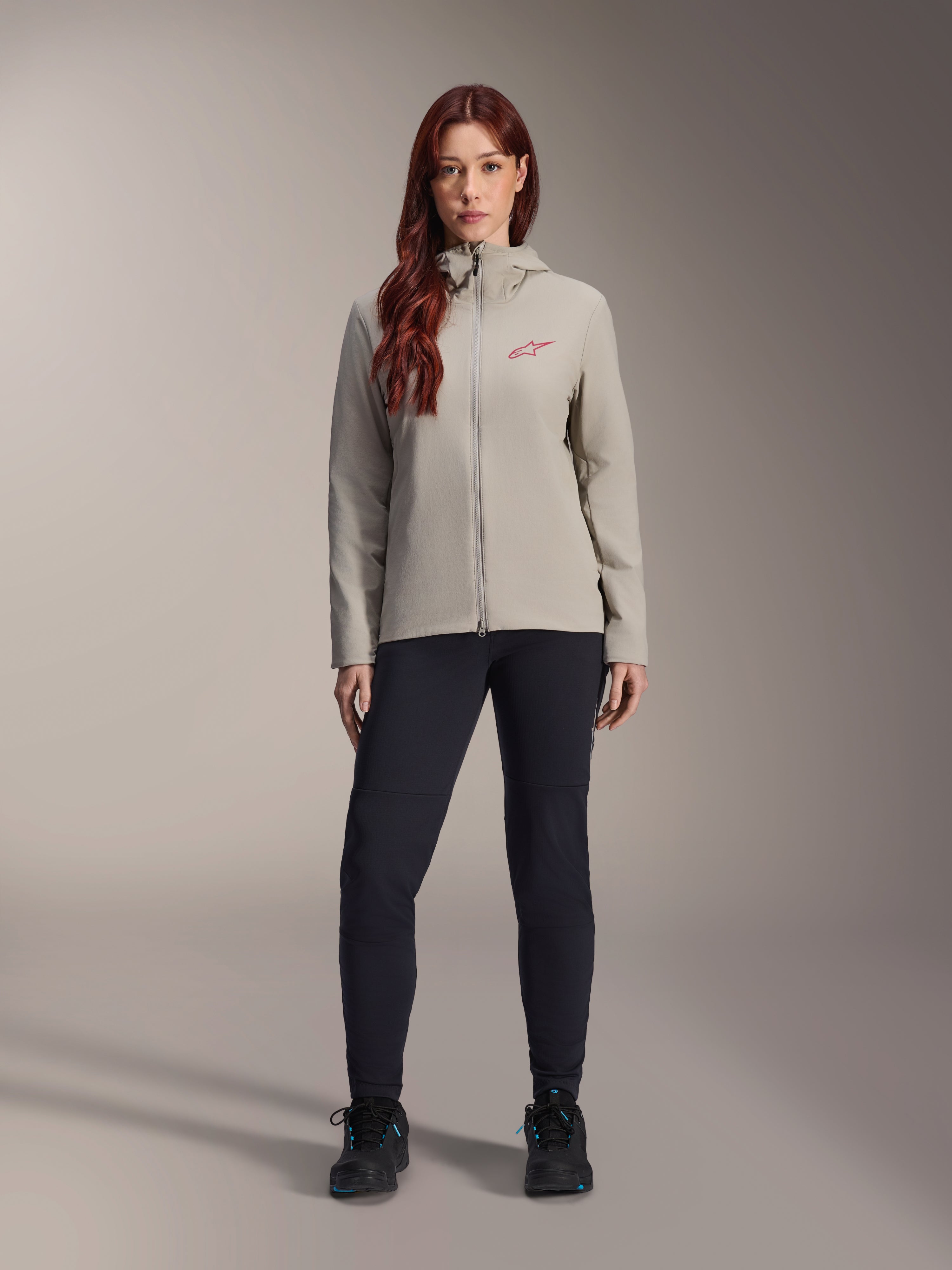 Giacca Termica Alpinestars Stella A-Dura da donna, giacca da mountain bike, grigio titanio, indossata con pantaloni tecnici neri e calzature nere, dotata di cappuccio foderato in pile e logo rosso sul petto, progettata per la guida in climi freddi