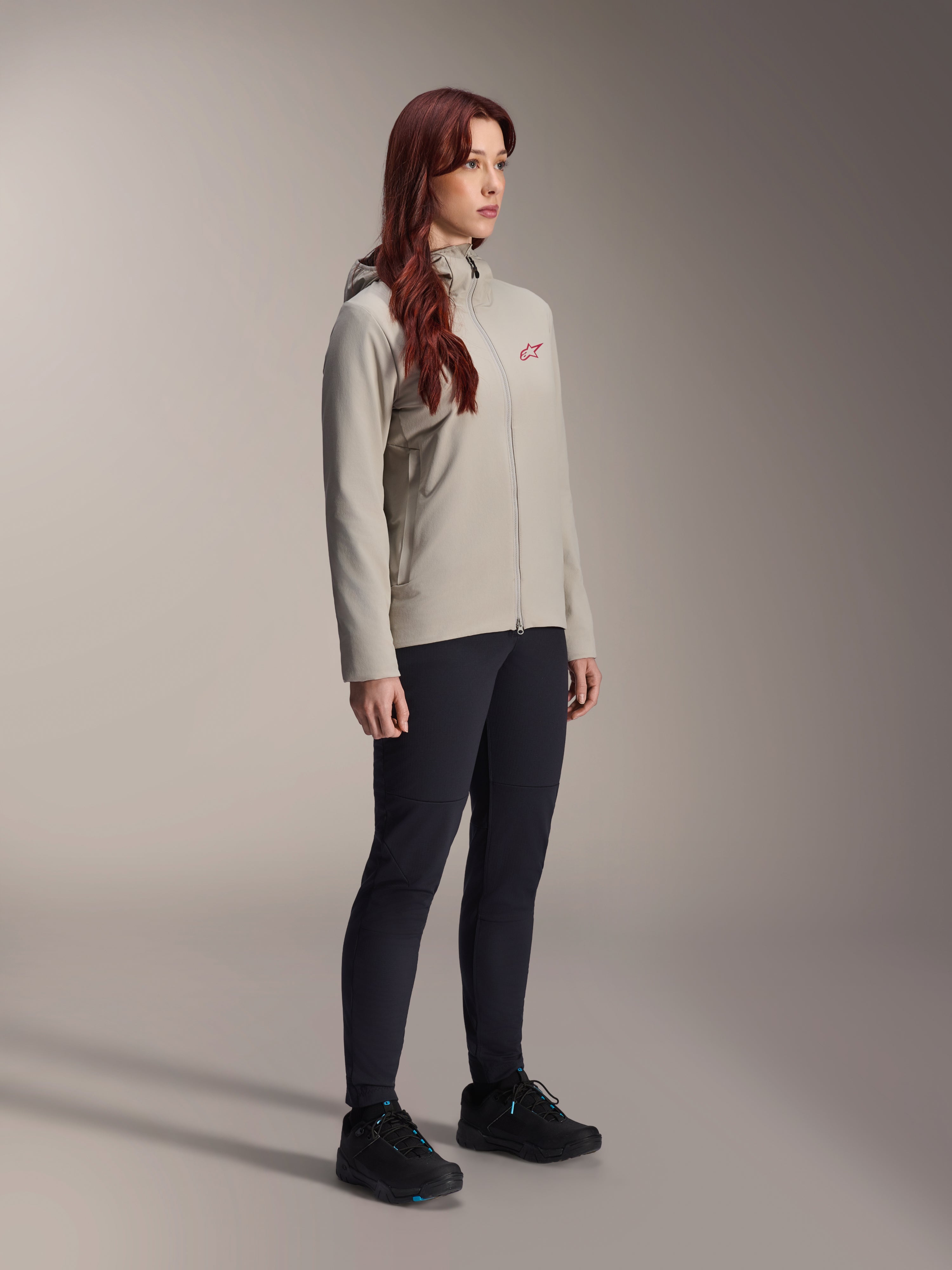 Giacca Termica Alpinestars Stella A-Dura, grigio titanio, giacca da ciclismo termica da donna con logo a stella rosso sul petto, indossata con pantaloni tecnici neri e scarpe da mountain bike nere, scatto in studio per abbigliamento da ciclismo