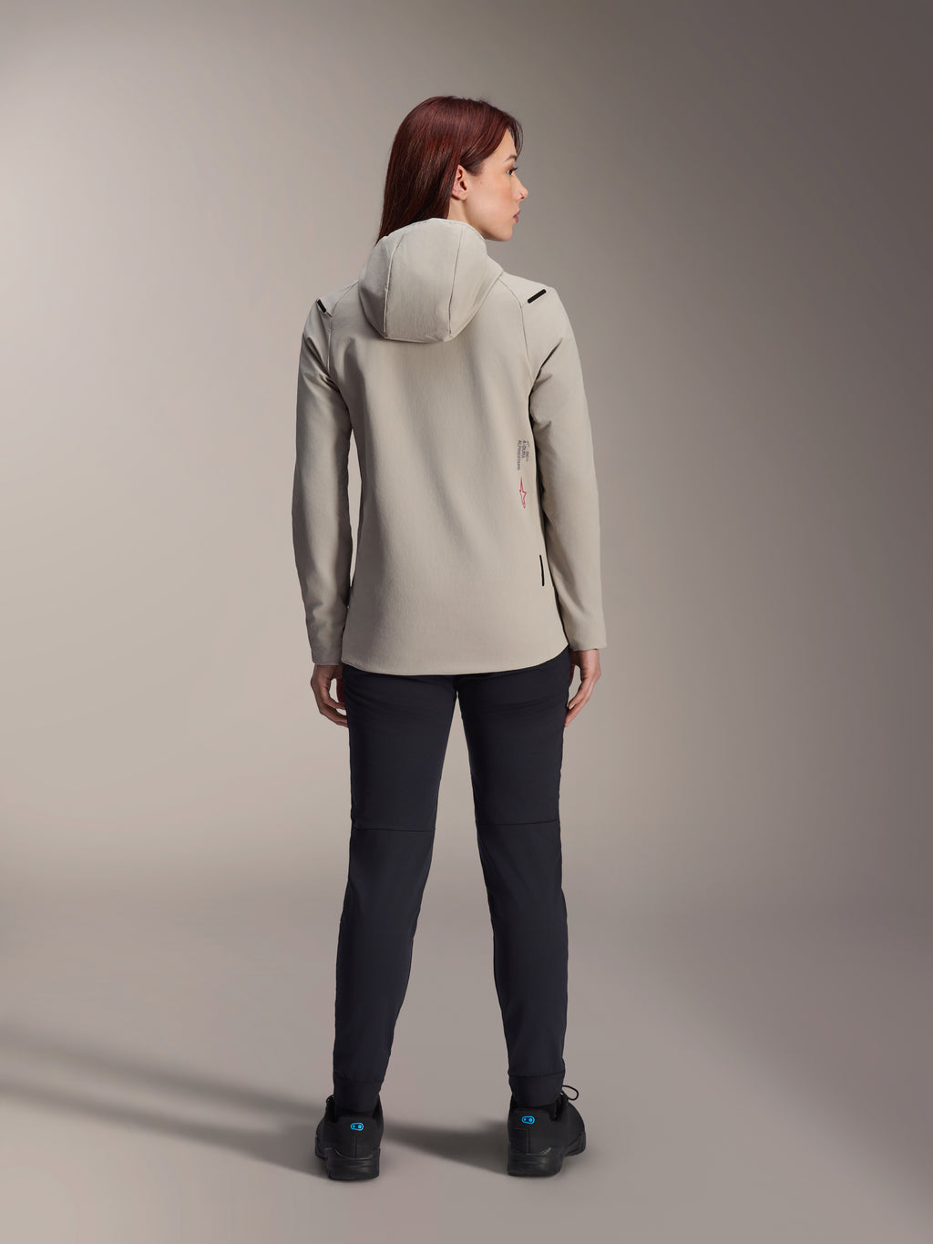 Giacca termica Stella A-Dura Alpinestars da donna, colore grigio titanio, vista posteriore indossata con pantaloni neri, dotata di cappuccio isolante foderato in pile e un piccolo logo rosso, giacca funzionale ed elegante per mountain bike in climi freddi.