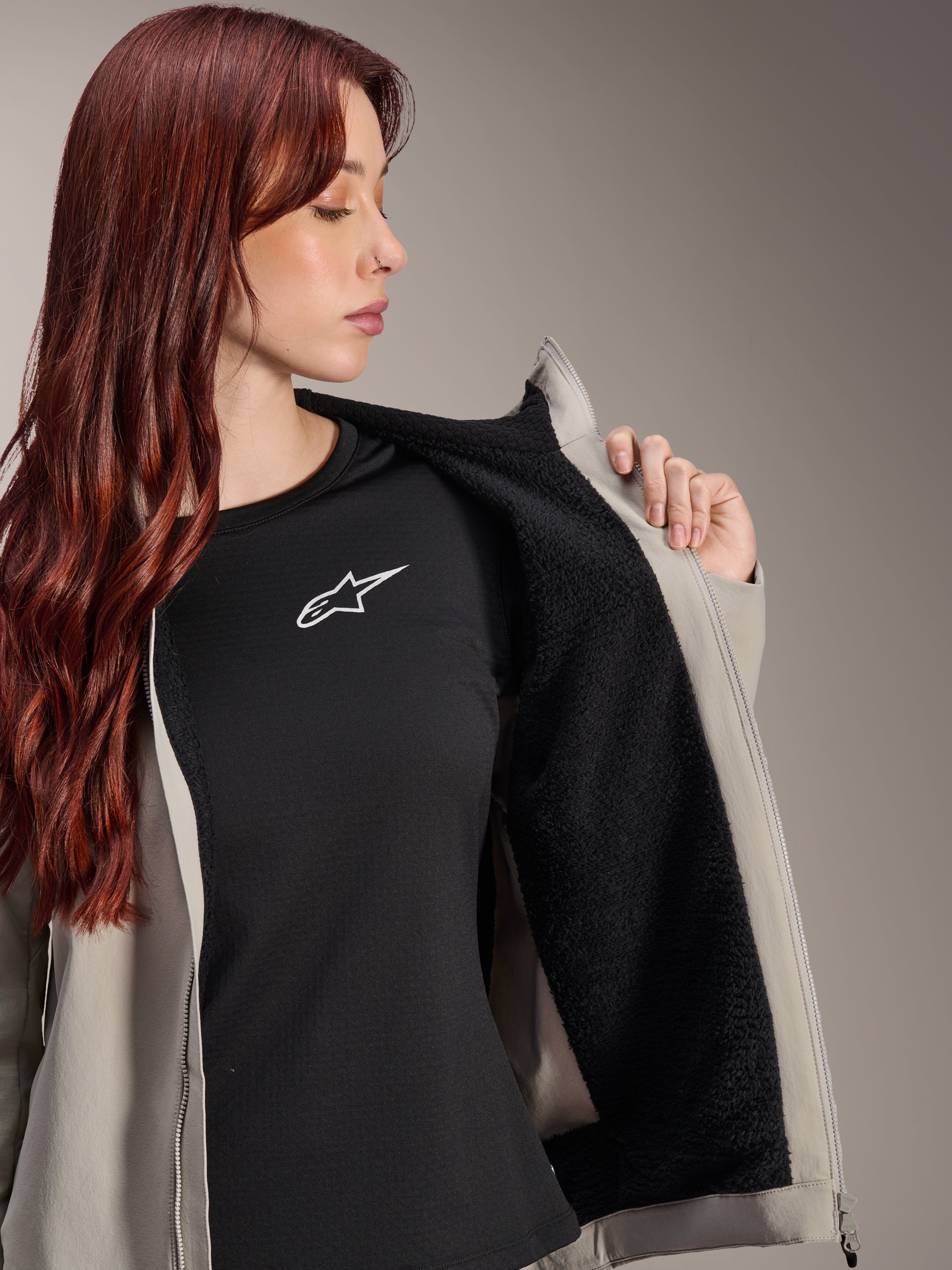 Donna che indossa la giacca termica Alpinestars Stella A-Dura in Titanium, che mostra la fodera in pile nero testurizzato, indossata sopra una t-shirt nera con logo a stella bianco, giacca leggera da mountain bike per condizioni fredde