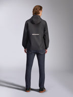 Giacca frangivento Alpinestars Speeder Chromium, nero, vista posteriore con marchio Alpinestars bianco al centro, modello con cappuccio, indossata da un modello con pantaloni in denim scuro, giacca casual ispirata al motorsport