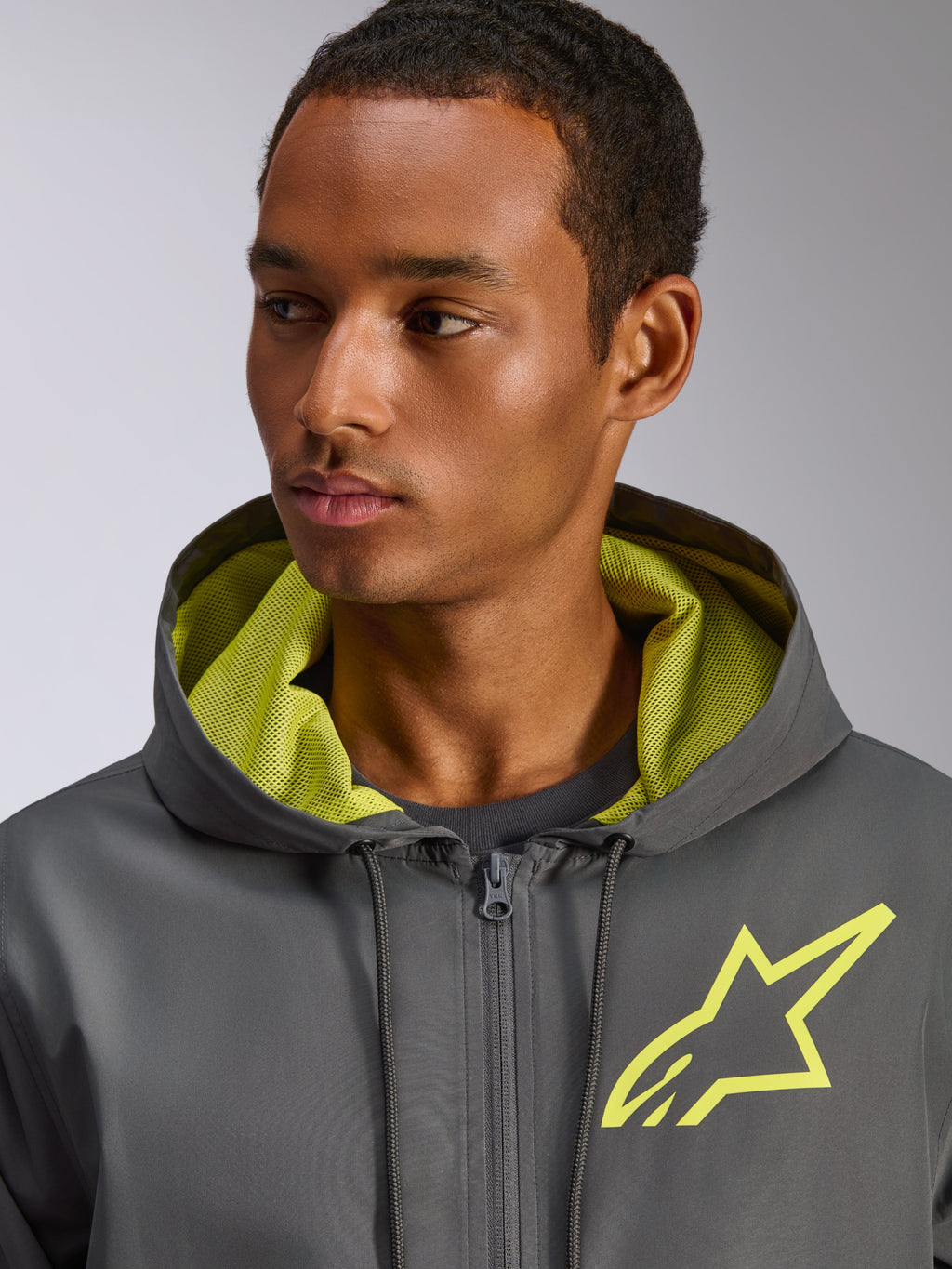 Giacca frangivento Alpinestars Speeder Chromium, grigio antracite con dettagli giallo Hi-Vis, caratterizzata da un logo a stella giallo sul petto e fodera del cappuccio in rete coordinata, giacca a vento casual leggera