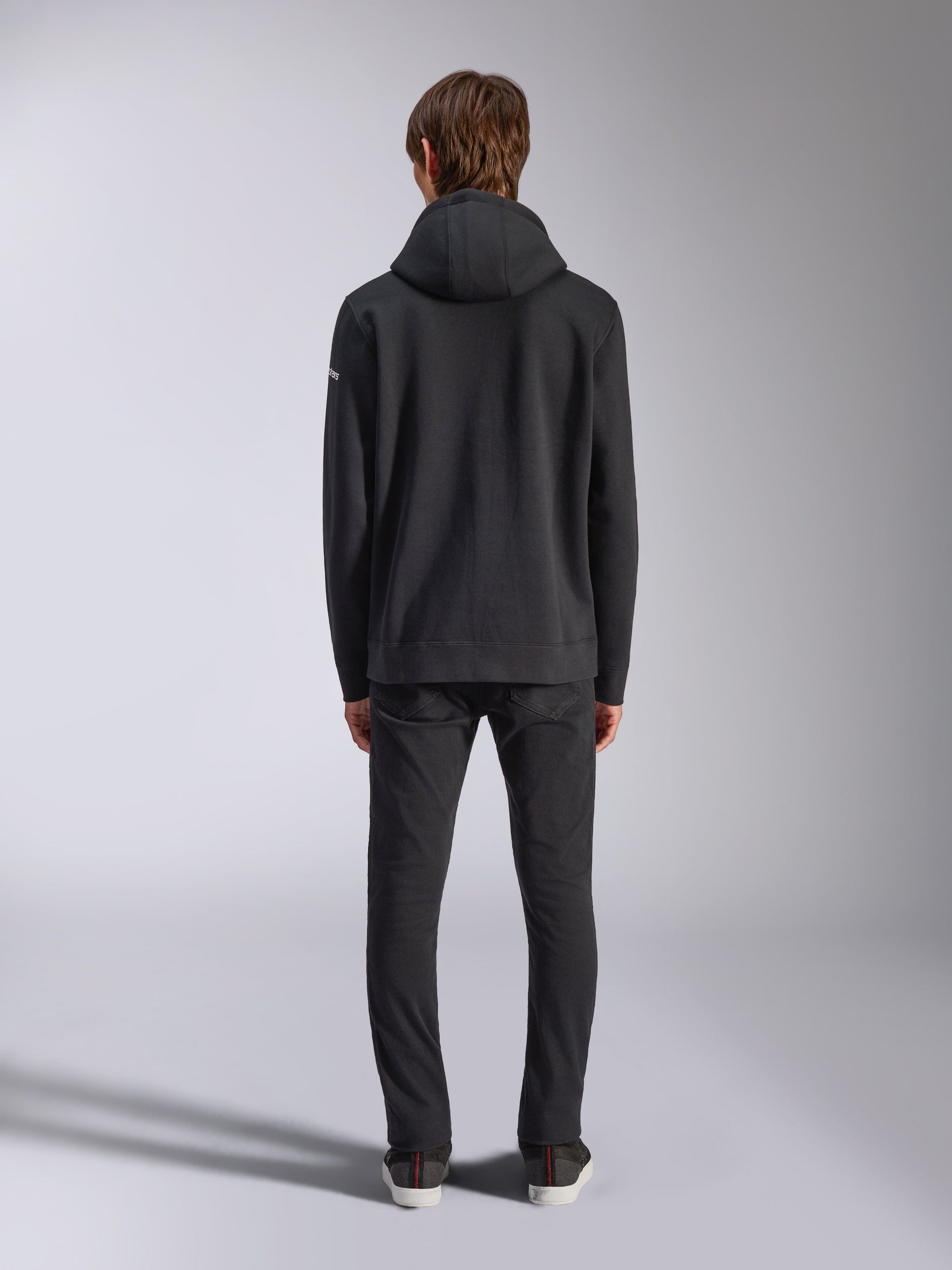 Alpinestars Frontal Hoodie, streetwear casual, nero, vista posteriore del modello che indossa una felpa con cappuccio in pile, con orlo e polsini a coste, piccolo logo wordmark bianco sulla manica, abbinata a pantaloni neri