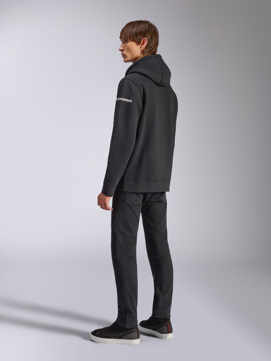 Alpinestars Felpa con cappuccio Frontal, streetwear casual, nero, vista laterale posteriore con logo wordmark bianco sulla manica, indossata con pantaloni neri e sneakers, design moderno ispirato al motorsport