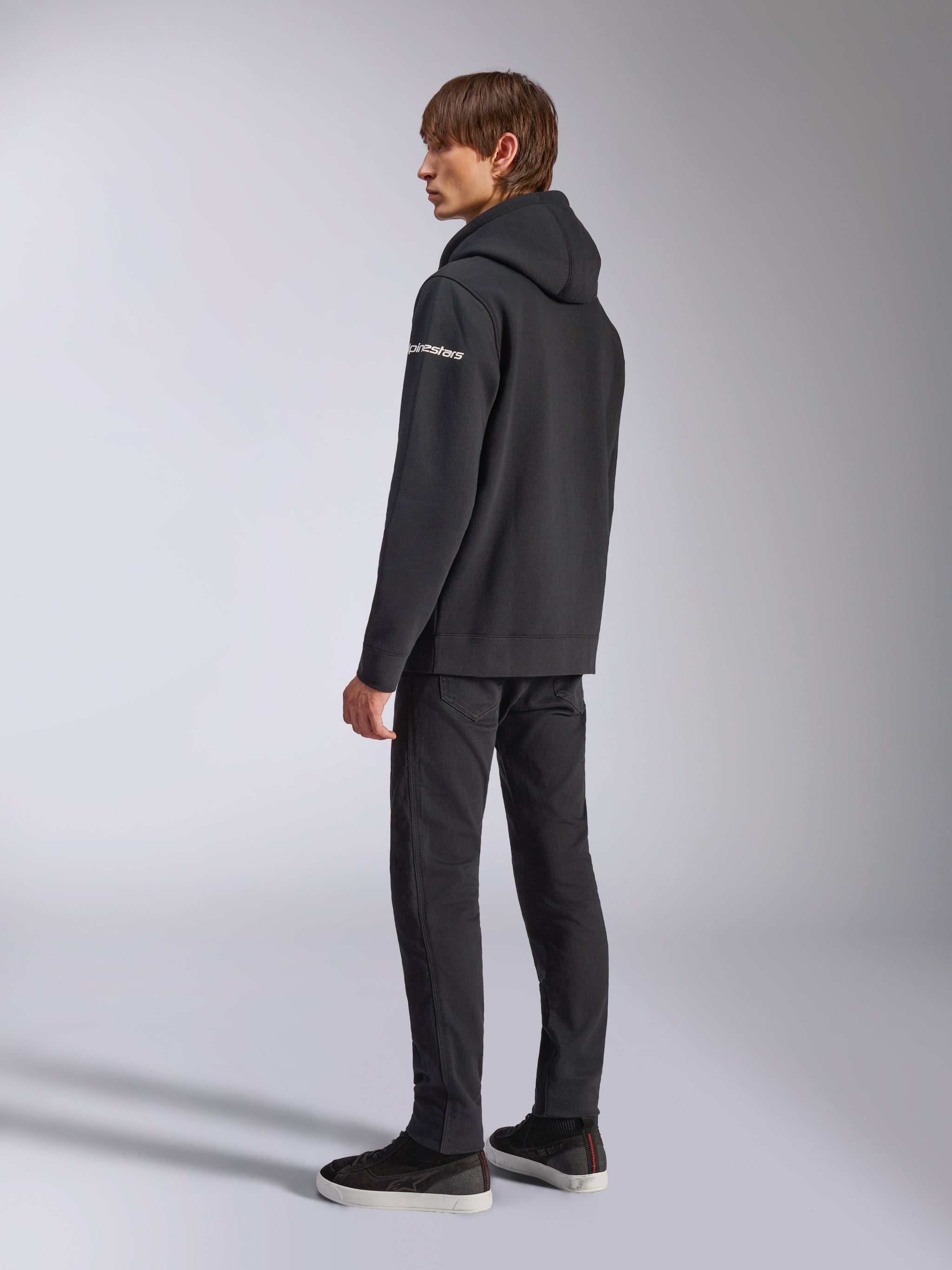 Alpinestars Felpa con cappuccio Frontal, streetwear casual, nero, vista laterale posteriore con logo wordmark bianco sulla manica, indossata con pantaloni neri e sneakers, design moderno ispirato al motorsport