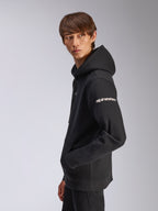 Alpinestars Felpa con cappuccio Frontal, felpa nera in pile, modello ritratto di profilo, logo Alpinestars bianco sulla manica, tasca a marsupio, streetwear casual ispirato al motorsport