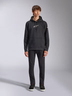 Alpinestars Frontal Hoodie, felpa pullover nera in pile, logo Alpinestars bianco sul petto e sulla manica, tasca a marsupio, cappuccio con cordino, indossata con pantaloni neri, design casual ispirato al motorsport