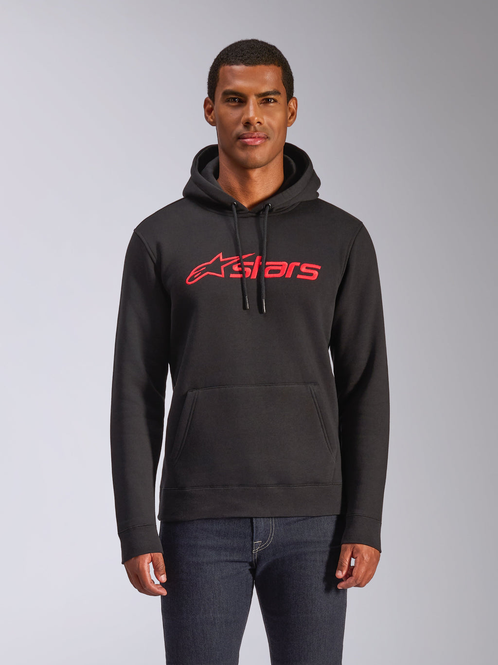Alpinestars Blaze V3 Hoodie, felpa da uomo in pile modello pullover, nera con logo Alpinestars rosso, indossata da un uomo con jeans scuri, dotata di cappuccio con cordino e tasca a marsupio, streetwear casual ispirato al motorsport