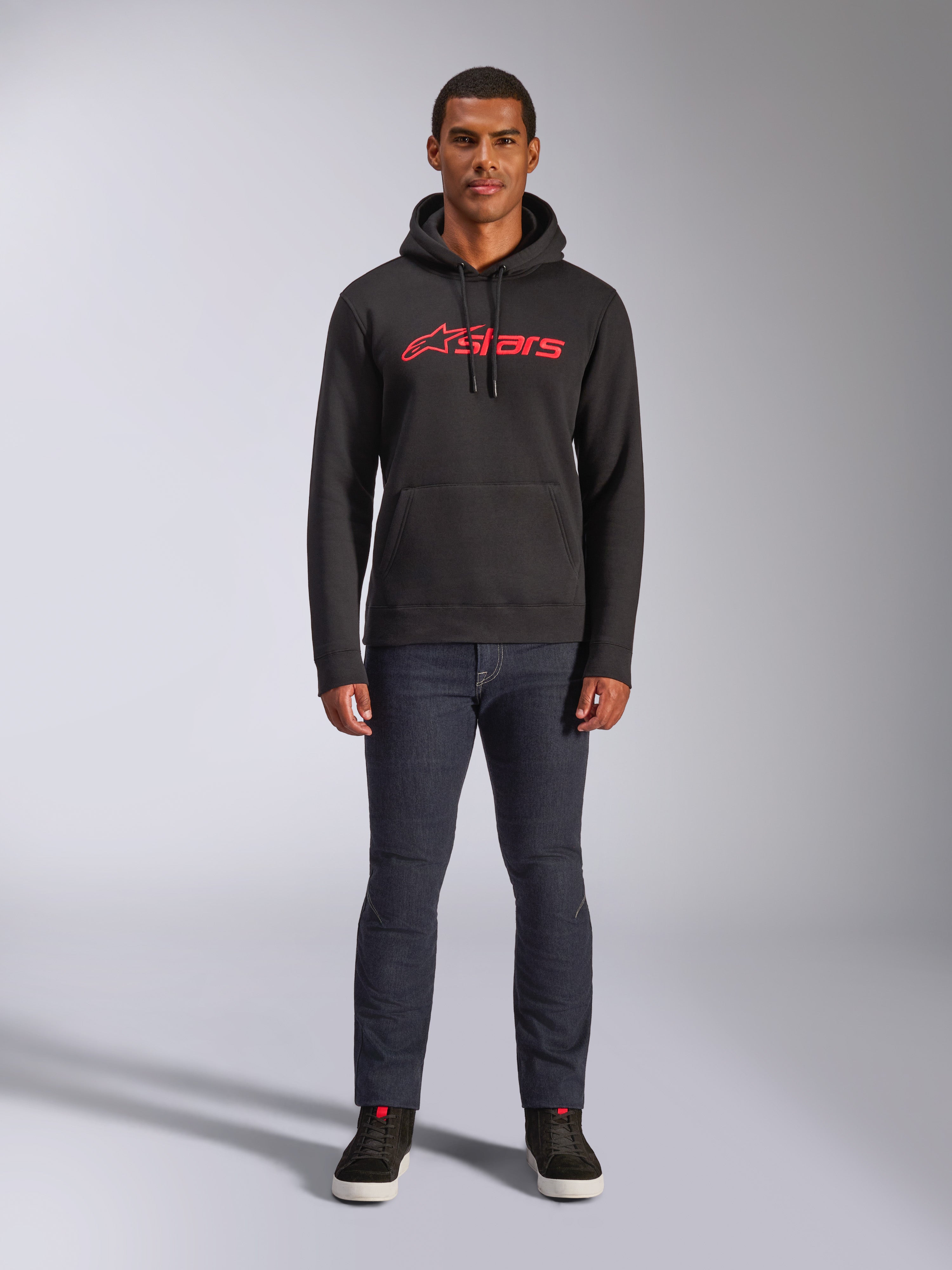 Felpa con cappuccio Alpinestars Blaze V3, streetwear casual, nero con logo Astars rosso, vista frontale, indossata da un modello con pantaloni in denim scuro e sneakers nere, design moderno in pile ispirato al motorsport