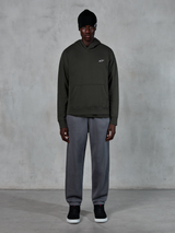 Modello che indossa la felpa con cappuccio Alpinestars Essentials Ageless, streetwear casual, Off Black con piccolo logo bianco sul petto, abbinata a joggers grigi, berretto nero e sneakers nere, design minimalista ispirato al motorsport