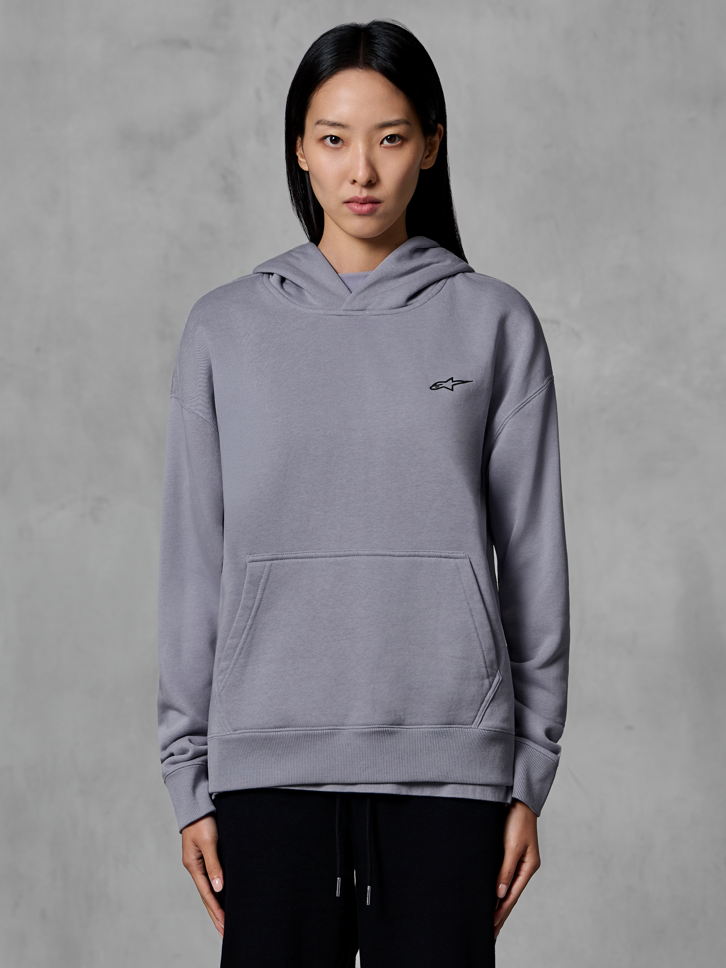 Felpa con cappuccio Alpinestars Essentials Ageless, abbigliamento sportivo casual, argento con piccolo logo nero, tasca a marsupio, pullover con cappuccio, indossata da una modella, abbigliamento lifestyle moderno