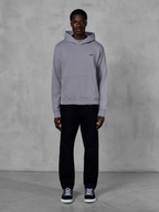 Alpinestars Essentials Ageless Hoodie, argento, modello uomo che indossa streetwear casual, piccolo logo Alpinestars nero sul petto, tasca a marsupio frontale, design minimalista, abbinata a pantaloni neri e sneakers