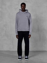 Alpinestars Essentials Ageless Hoodie, argento, modello uomo che indossa streetwear casual, piccolo logo Alpinestars nero sul petto, tasca a marsupio frontale, design minimalista, abbinata a pantaloni neri e sneakers