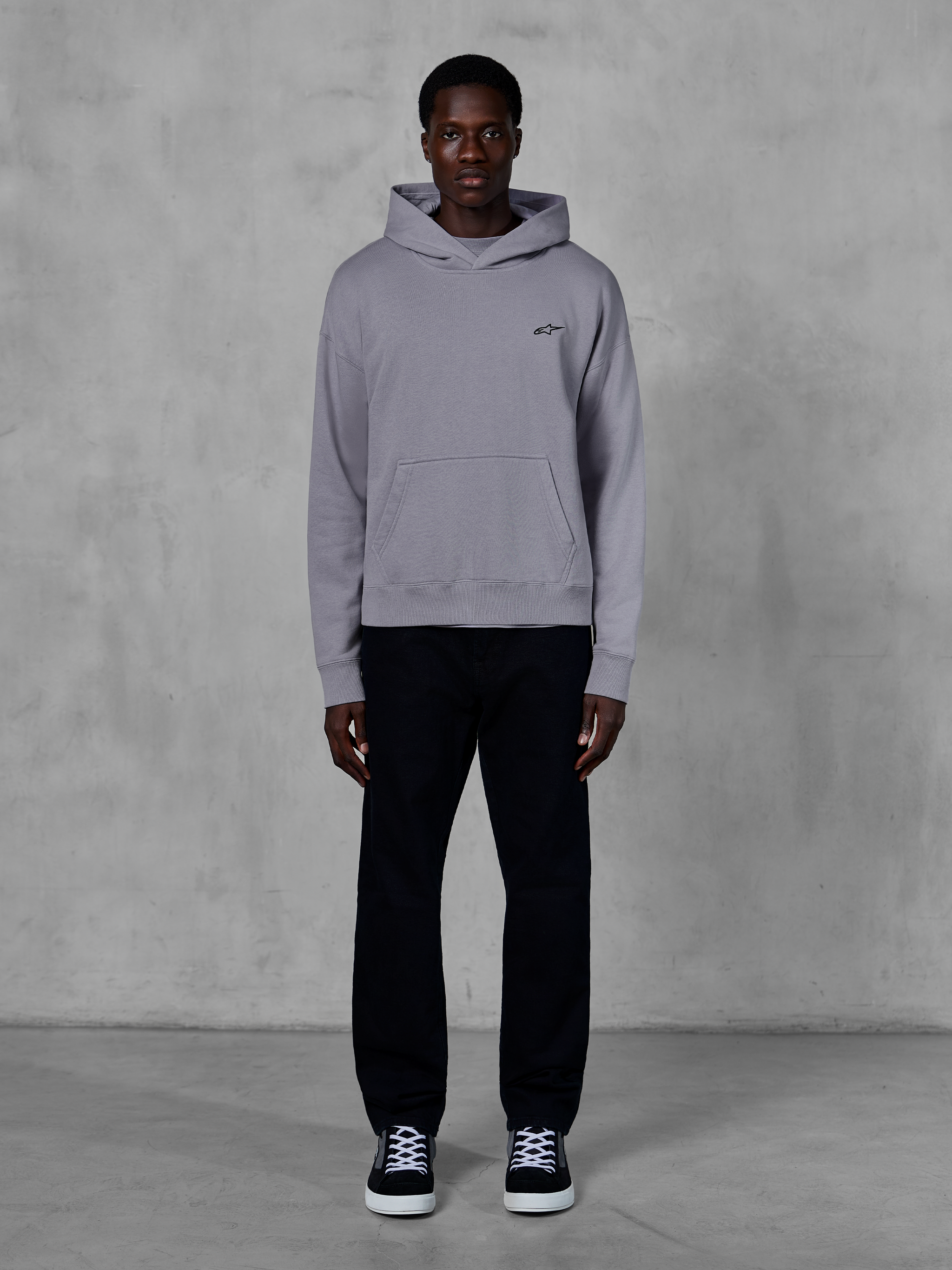 Alpinestars Essentials Ageless Hoodie, argento, modello uomo che indossa streetwear casual, piccolo logo Alpinestars nero sul petto, tasca a marsupio frontale, design minimalista, abbinata a pantaloni neri e sneakers