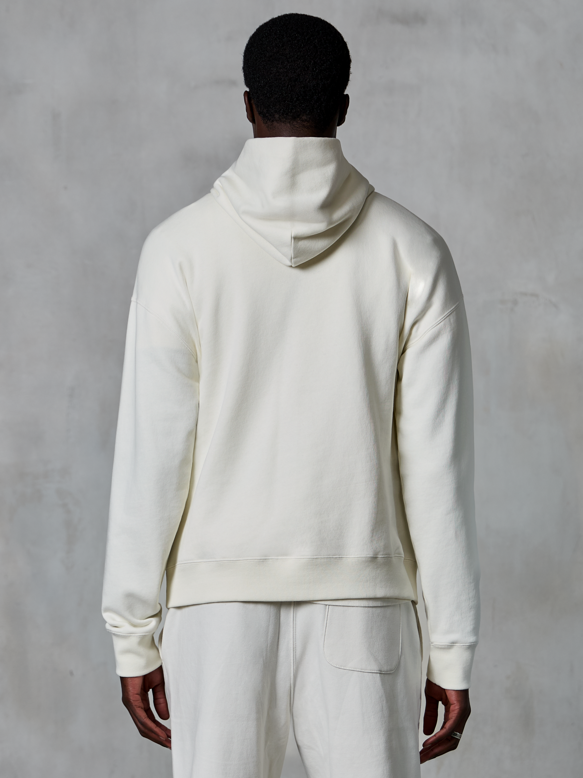 Alpinestars Essentials Ageless Hoodie, felpa con cappuccio pullover off-white, vista posteriore su modello, design pulito e minimalista, pantaloni casual coordinati, vestibilità rilassata per il comfort quotidiano