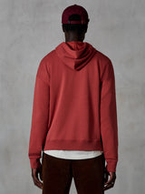 Alpinestars Essentials Ageless Hoodie, felpa casual in pile, rosso mattone, vista posteriore del modello che indossa abbigliamento lifestyle, caratterizzata da un design pulito con orlo e polsini a costine, abbinata a pantaloni in velluto a coste marroni e un berretto bordeaux