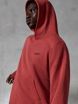 Alpinestars Essentials Ageless Hoodie, abbigliamento sportivo casual, rosso mattone, indossata da un modello con cappuccio sollevato, con un piccolo logo nero ricamato, morbida texture in pile, stile streetwear con vestibilità rilassata