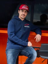 Felpa con cappuccio Alpinestars Formulation, blu navy, felpa con zip frontale e logo Alpinestars sul petto, indossata con cappellino rosso e jeans, abbigliamento streetwear casual stile motorsport