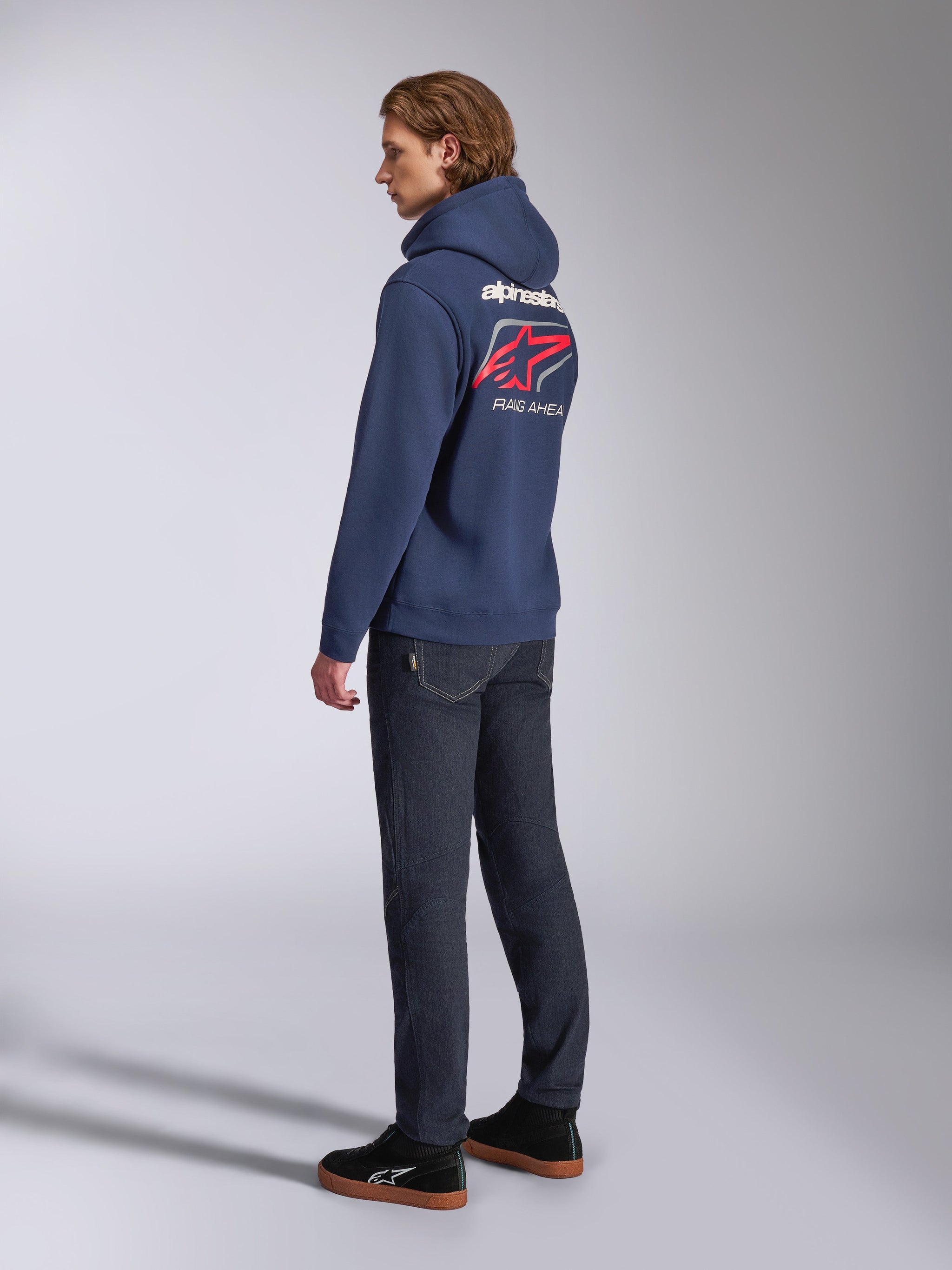 Alpinestars Formulation Hoodie, blu navy, vista posteriore con scritta Alpinestars bianca e logo Astars rosso con testo 'RACING AHEAD', indossata con jeans scuri e sneakers nere, abbigliamento lifestyle casual ispirato al motorsport