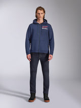 Felpa con cappuccio Alpinestars Formulation, felpa in pile blu navy con zip, indossata da un modello con jeans blu scuro, logo rosso e bianco sul petto, cappuccio foderato in rete con cordini, streetwear casual motorsport