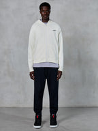 Alpinestars Essentials Ageless Zip Hoodie, felpa con zip integrale bianco panna, vestibilità rilassata con piccolo logo nero sul petto, indossata con pantaloni della tuta neri e sneakers, streetwear casual ispirato al motorsport.
