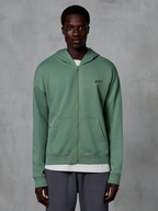 Alpinestars Essentials Ageless Zip Hoodie, felpa casual streetwear con zip, verde Cactus, con un discreto logo ricamato sul petto, tasche a marsupio divise e polsini a costine, indossata da un modello su uno sfondo grigio testurizzato