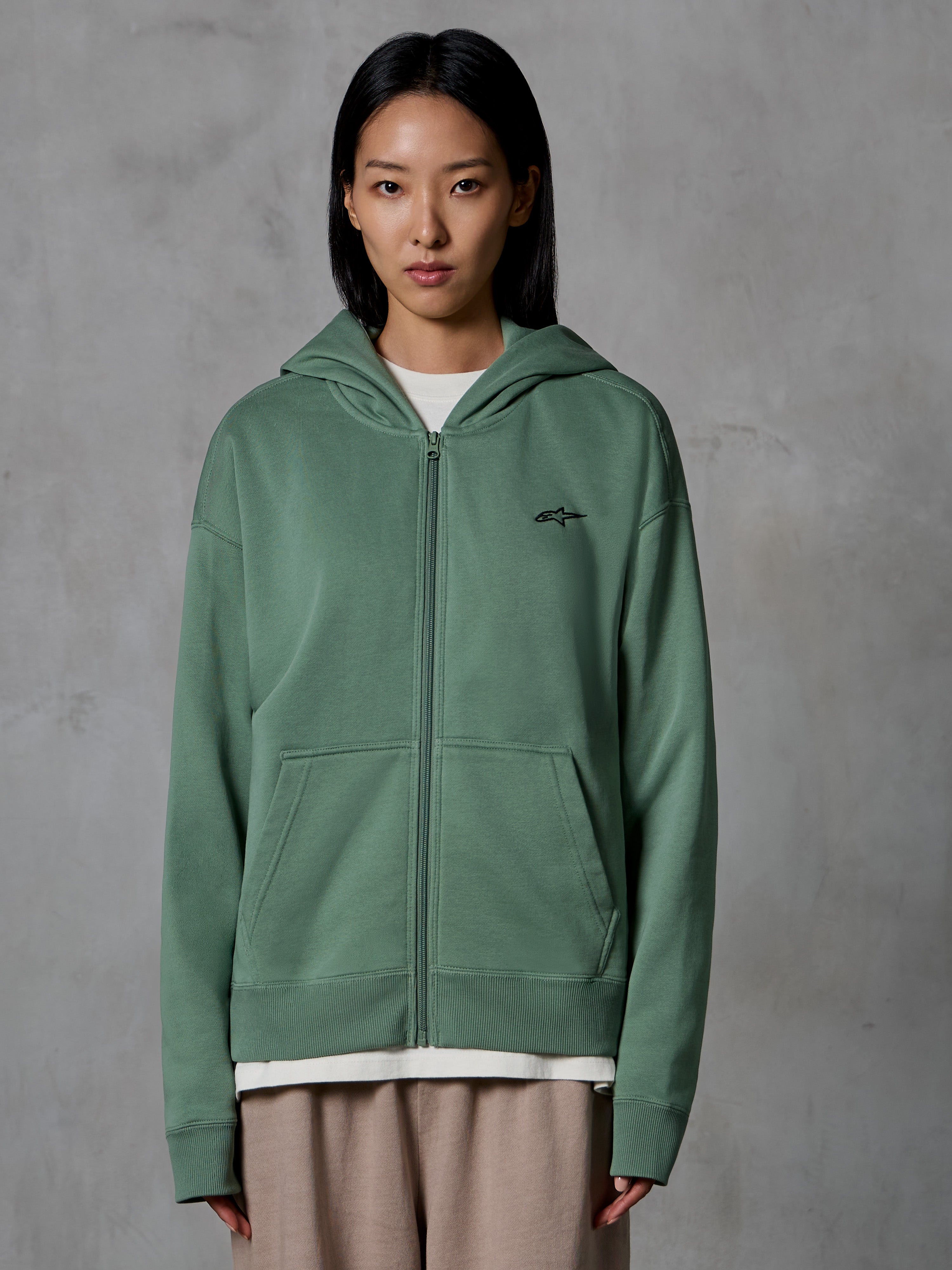 Felpa con cappuccio e zip Alpinestars Essentials Ageless, Verde Cactus, streetwear casual indossato da una modella, felpa in pile con zip e piccolo logo nero sul petto, tasche anteriori, vestibilità rilassata per l'uso quotidiano
