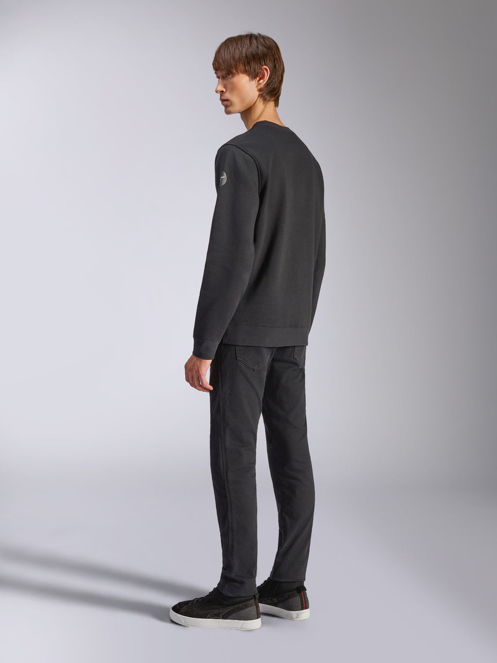 Alpinestars Bettern Crew, felpa girocollo in pile, nero, modello maschile inquadrato di schiena e di lato, con polsini e orlo a coste e un piccolo logo sulla manica, abbigliamento casual streetwear ispirato al motorsport