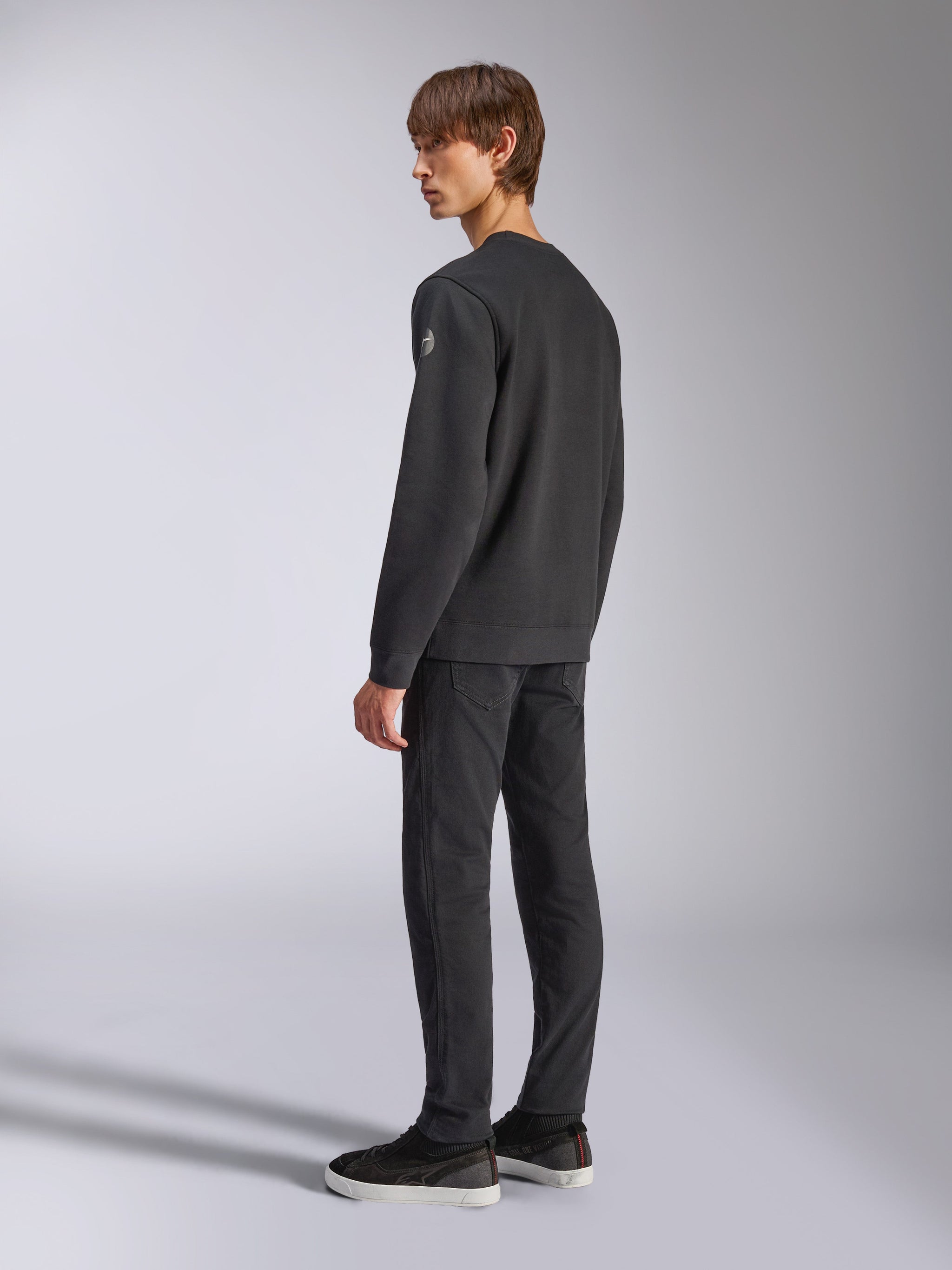 Alpinestars Bettern Crew, felpa girocollo in pile, nero, modello maschile inquadrato di schiena e di lato, con polsini e orlo a coste e un piccolo logo sulla manica, abbigliamento casual streetwear ispirato al motorsport