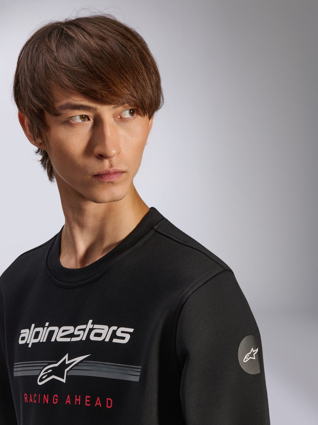 Alpinestars Bettern Crew, felpa a girocollo nera con logo Alpinestars bianco, strisce grigie e scritta rossa 'RACING AHEAD', logo a stella circolare sulla manica, streetwear casual ispirato al motorsport