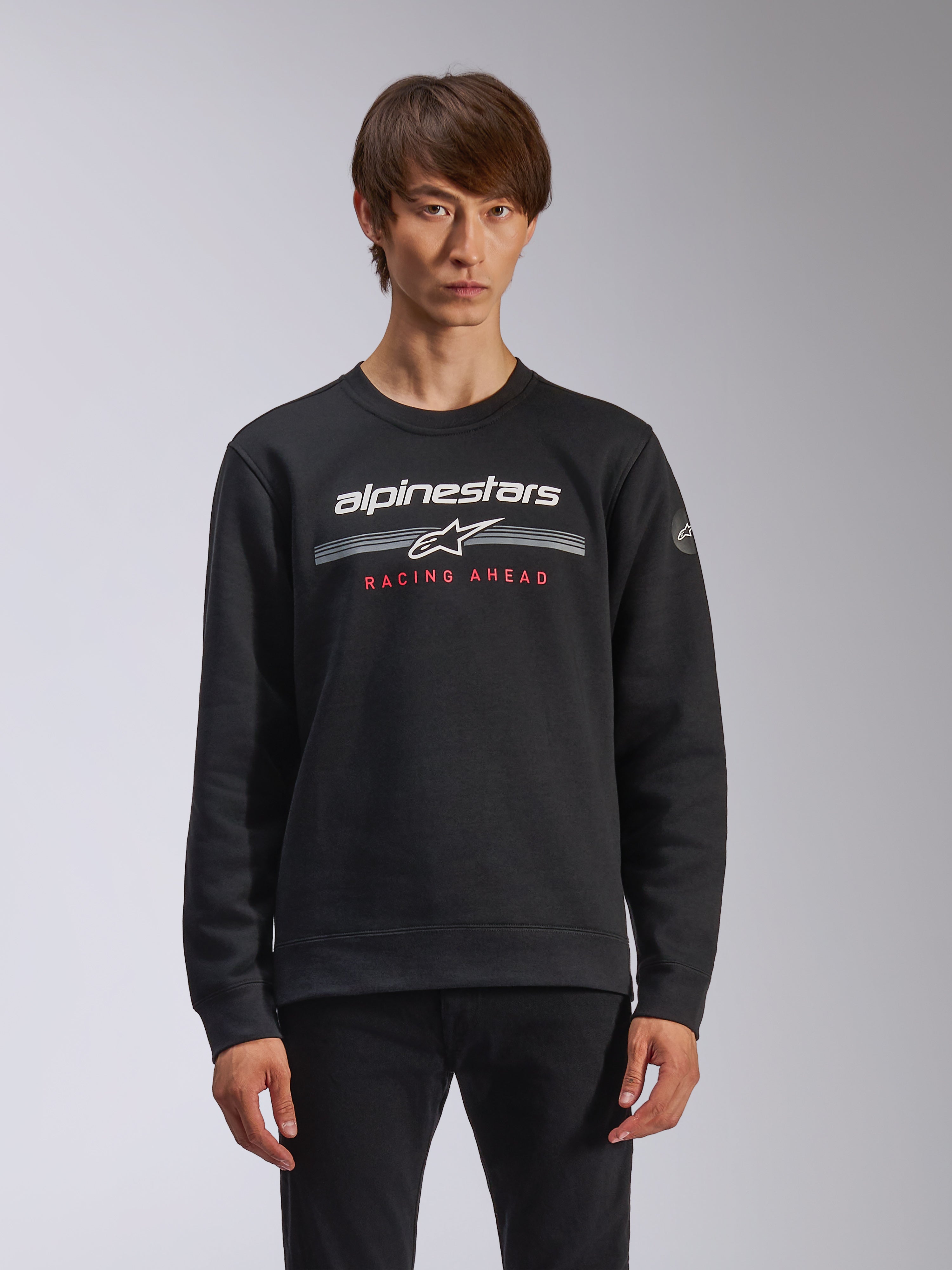 Alpinestars Bettern Crew, felpa a girocollo, nero, con marchio Alpinestars bianco, strisce orizzontali grigie e scritta 'RACING AHEAD' rossa, streetwear casual ispirato al motorsport
